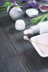 different cosmetic creams, bath salt, soap, anti aging serum pipette with fresh lavender flowers on black wooden texture
