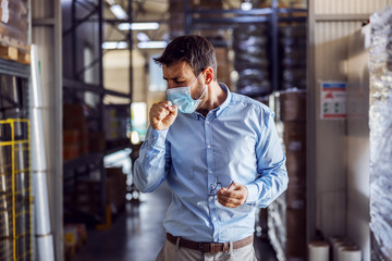 Full length of handsome smiling businessman having phone call with customer while walking in warehouse.