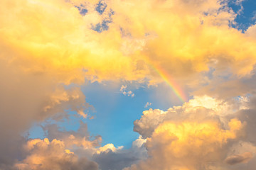 Yellow orange sun light on bright clouds in blue sky with Little rainbow