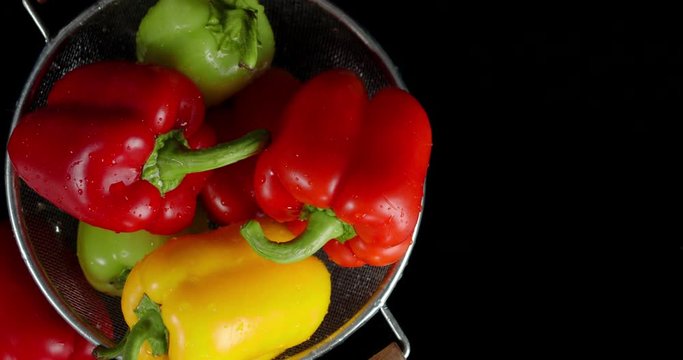 Various sweet peppers in a colander falling water drops.