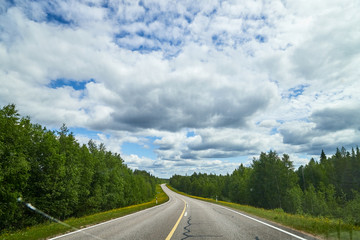 View from relief car windscreen on the blue sky with white clouds, grey asphalt road and landscape with forest and green teeses. Landscape through window