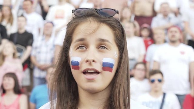 Female football fan sings Russian national anthem cheering at match, supporting football team. Slow motion of Young woman listening and singing national anthem before football match at fan zone