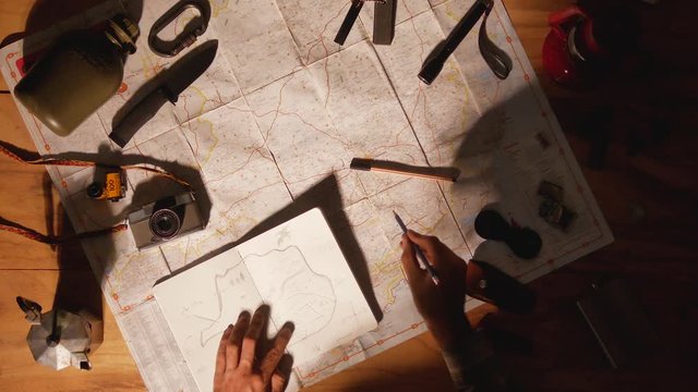 Man drawing map on his rustic table with camping accessories