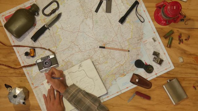 Man drawing map on his rustic table with camping accessories