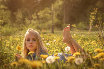 Glückliches Kind liegt im Frühling auf einer Blumenwiese mit Pusteblumen und pflückt einen...