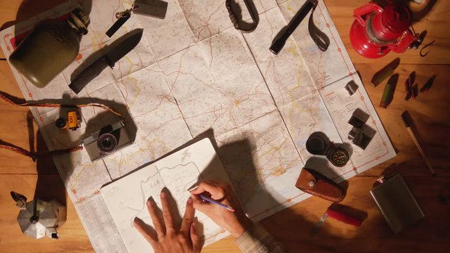 Man drawing map on his rustic table with camping accessories