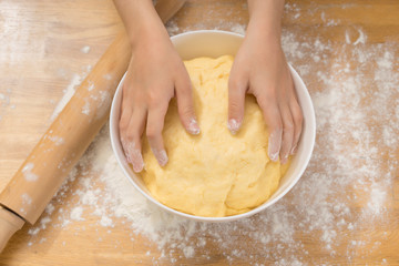 The girl's hands with a dough and rolling pin on a wooden table . Close up.