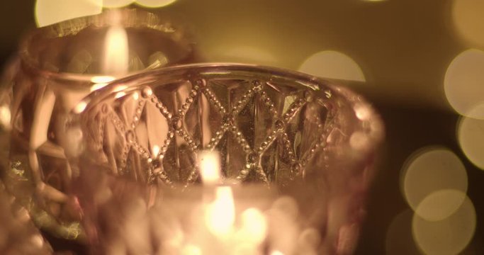 Close up of a tealight candle in a glass purple candle holder with bokeh background.