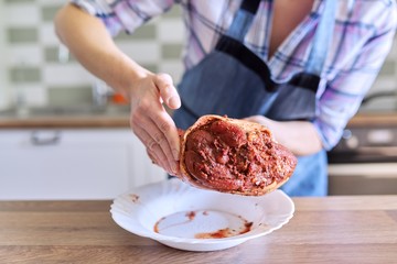 Female housewife in apron cooking meat at home in the kitchen