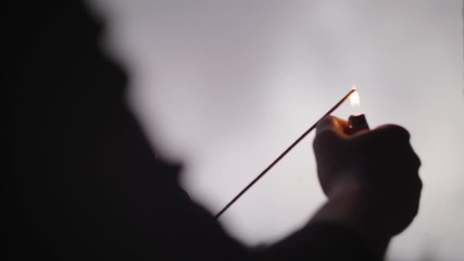 Lighting incense with a lighter. Close up, slow-motion, handheld.