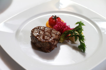 Serving a steak on a white plate with tomato, vegetables garnish. Fancy dinner main course, steak with grill marks .