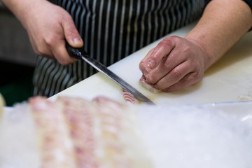 Chef cutting a fresh slices of salmon sashimi with a sharp knife.