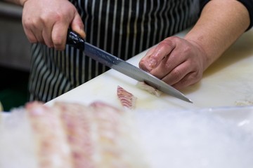Professional chef cutting a fresh slices of salmon sashimi with a sharp knife. Japanese fresh seafood.