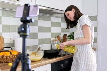 Teenager girl, food blogger cooking pancakes with orange at home in kitchen