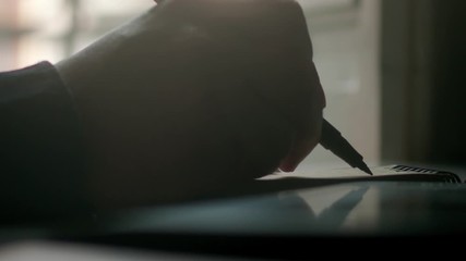 Extreme close up of a man writing and designing with his hand and a pen on a paper notebook in super slow motion on a desk table at the home studio during the day detail shot