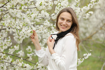 happy beautiful girl took off her medical mask to breathe in the smell of flowers. A girl in a mask stands in blossoms. the end of quarantine