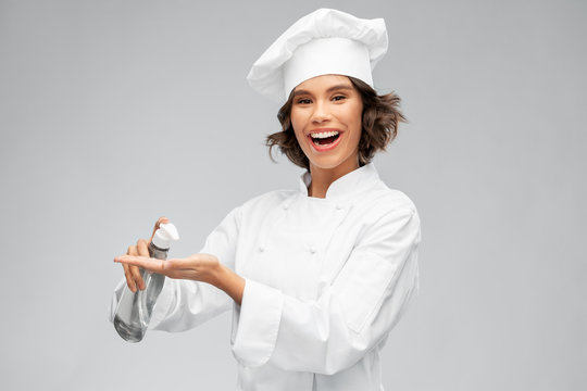 cooking, culinary and people concept - happy smiling female chef in toque with hand sanitizer or liquid soap over grey background