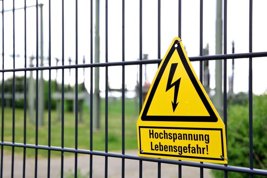 fence with safety instructions. Sign: Hochspannung - Lebensgefahr, engl. High voltage - Danger to life. High-voltage switchgear on blurred background 