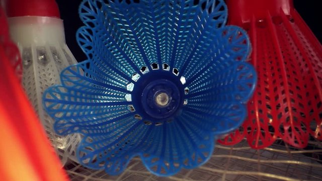 A red badminton birdie on its side, moving past it towards three others, & pushing deep inside center blue one. Great macro of the plastic mesh and its patterns, it rolls left at the end.