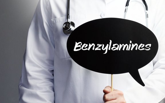 Benzylamines. Doctor in smock holds up speech bubble. The term Benzylamines is in the sign. Symbol of illness, health, medicine