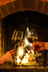 Two glasses of white wine in hand on the background of a burning fireplace