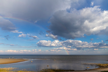 Obraz premium Rainbow over the sea with cloudy skies on a sunny day in spring.