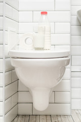 Lactose intolerance. Glass of milk, a bottle of dairy product and a roll of toilet paper are on the toilet bowl. Vertical photo.