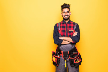 Fototapeta na wymiar portrait of indian happy handyman with tool belt isolated on yellow background