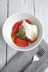 Tomatoes, pesto and stracciatella cheese in a white bowl in the background
