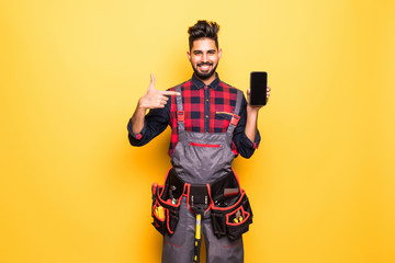 Portrait of smiling indian handyman showing screen of mobile phone on yellow background