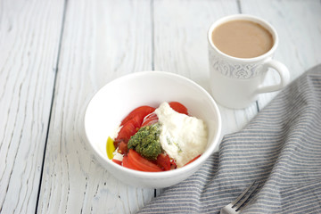 Tomatoes, pesto and stracciatella cheese in a white bowl in the background
