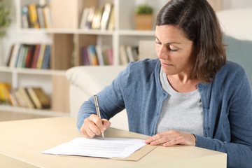Serious adult woman signing document at home