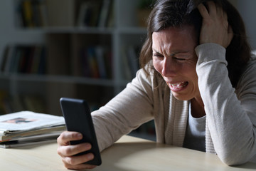 Sad adult woman crying reading news on phone at night at home