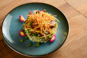 Traditional Russian salad Olivier served on a blue plate over light rustic wooden table.