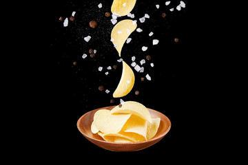 Falling potato chips into wooden plate filled with chips isolated on black background