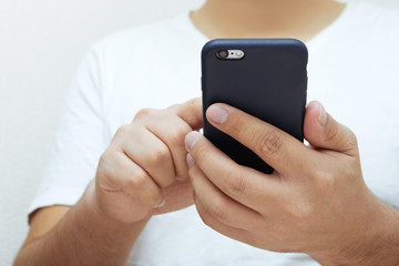 Close-up of a young man holding a smartphone and tapping the screen. Concept of modern electronics and technologies for business and education