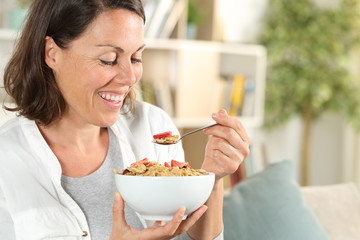 Happy adult woman eating cereal bowl having breakfast at home