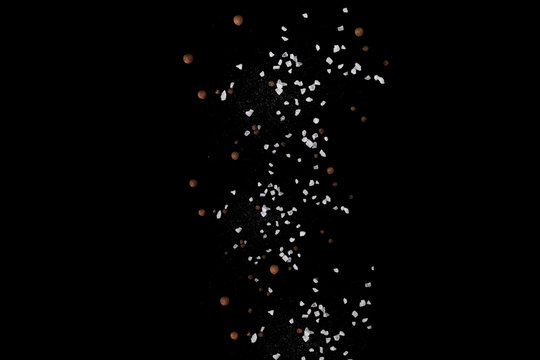 Levitating salt crystals and black pepper spice on black. Copy space