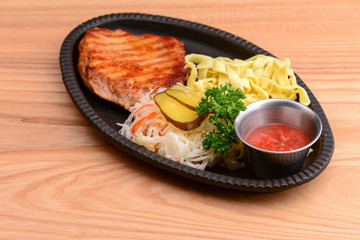 Grilled steak with vegetables and tomato sauce served on a black plate over light rustic background.