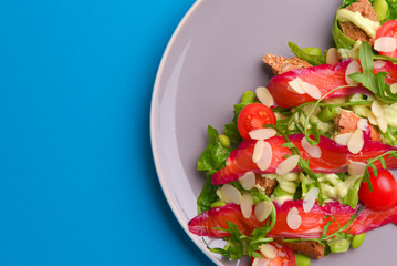 Fresh salad with smoked salted salmon, tomatoes and pumpkin seeds. Served on a gray plate over gray texture background.