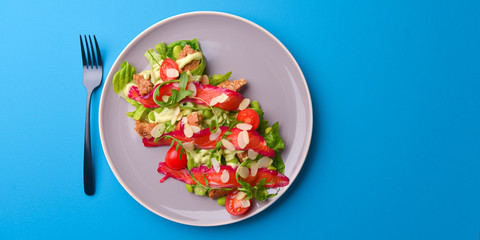 Fresh salad with smoked salted salmon, tomatoes and pumpkin seeds. Served on a gray plate over gray texture background.