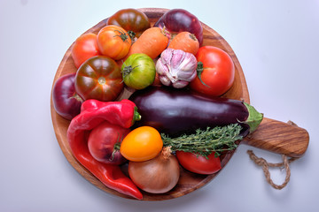 Fresh red, purple, yellow, orange tomatoes, carrots, red peppers, thyme, aubergine, onion, garlic on a wooden plate.