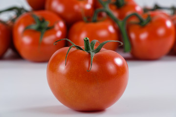 Eine einzelne rote reife Tomate im Vordergrund, dahinter eine Menge anderer Tomaten (Rispentomaten)