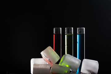 Colorful shot drinks in glass tubes and ice cubes around. Contrast image on a dark background, copy space