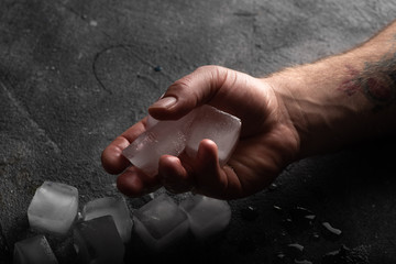 Bunch of ice cubes in man's hands and on a table. Atmospheric low key image
