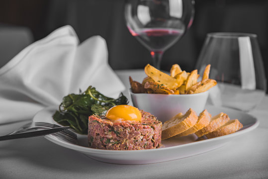 Steak tartare with wedges, vegetables and bread as a side dishes served with red wine  