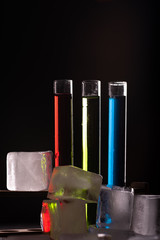 Colorful shot drinks in glass tubes and bunch of ice cubes. Dark background, atmospheric bar image