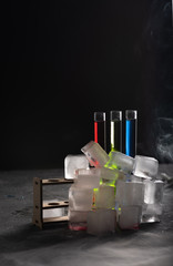 Colorful shot drinks in glass tubes, smoke or steam around and bunch of ice cubes. Dark background, atmospheric bar image
