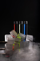 Colorful shot drinks in glass tubes and ice cubes around. Contrast image on a dark background, copy space