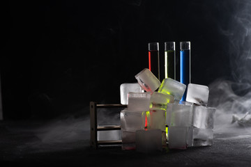 Colorful shot drinks in glass tubes with smoke or steam around and ice cubes. Dark background, atmospheric bar image with copy space